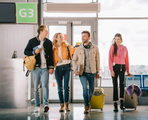smiling young friends with documents and luggage in airport term
